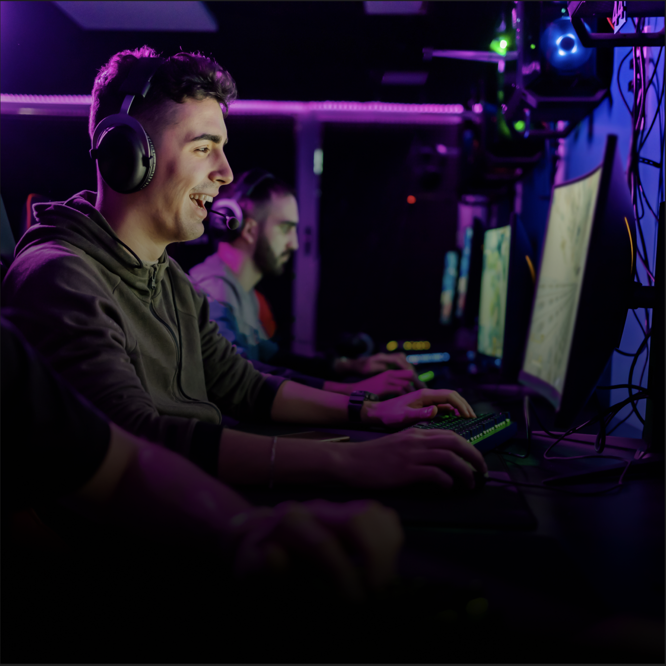 Two gamers wearing headsets smiling at their PCs in a purple-lit esports lounge